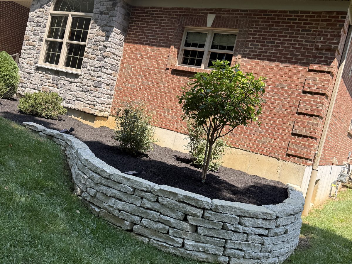 Landscaping before and after in Cincinnati showing a finished block retaining wall holding the slope
